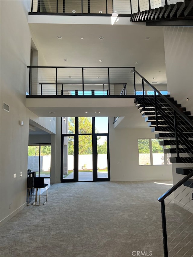 stairway featuring a towering ceiling, carpet floors, and a healthy amount of sunlight