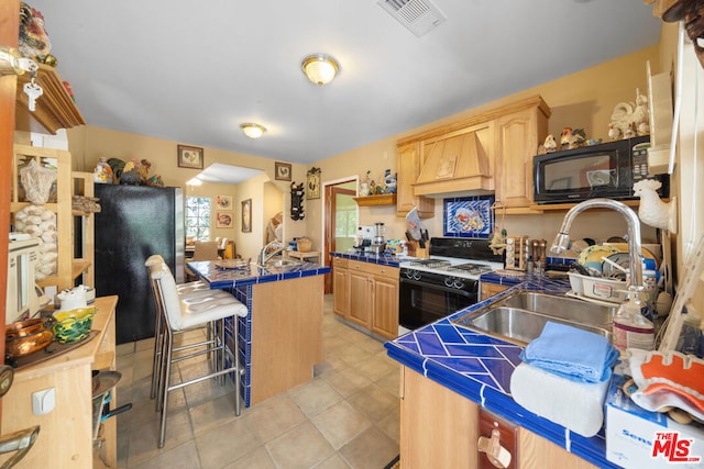 kitchen with a kitchen bar, custom range hood, sink, black appliances, and tile counters