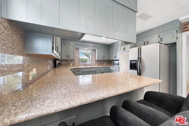 kitchen with a breakfast bar area, kitchen peninsula, decorative backsplash, and refrigerator with ice dispenser