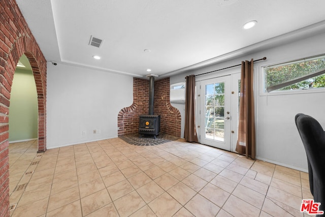 unfurnished living room with a wood stove, light tile patterned flooring, and brick wall