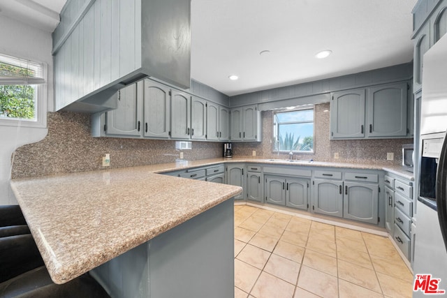 kitchen featuring kitchen peninsula, decorative backsplash, light tile patterned floors, and gray cabinetry