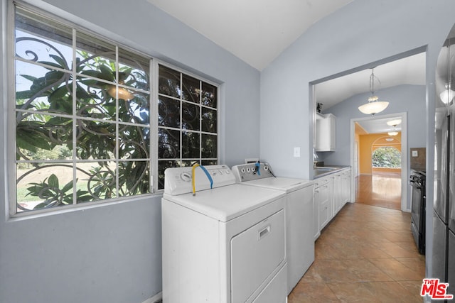 clothes washing area with washing machine and dryer, plenty of natural light, light tile patterned flooring, and cabinets