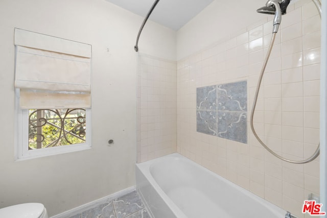 bathroom featuring tile patterned flooring, toilet, and tiled shower / bath