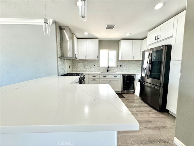 kitchen featuring appliances with stainless steel finishes, white cabinetry, beverage cooler, and wall chimney range hood