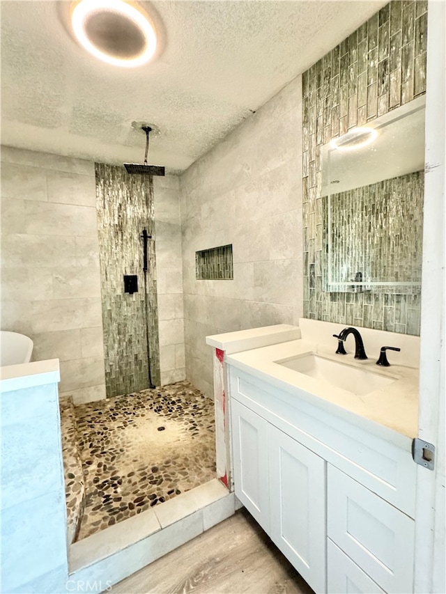 bathroom featuring vanity, tiled shower, wood-type flooring, a textured ceiling, and tile walls