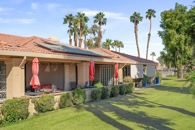 back of house with a patio, a yard, and solar panels