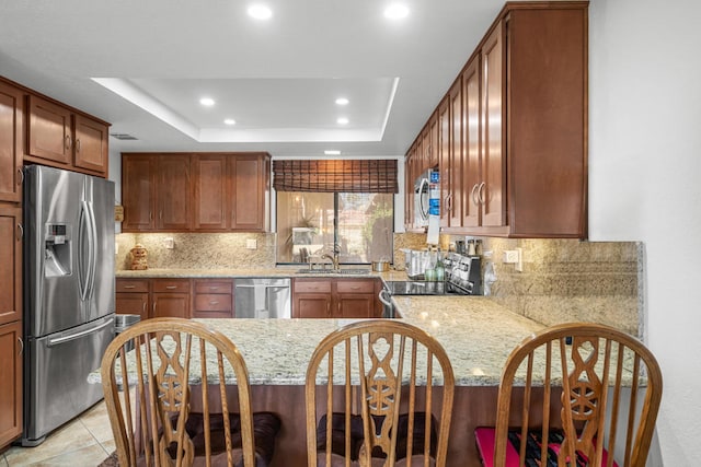 kitchen with light stone counters, a raised ceiling, kitchen peninsula, backsplash, and stainless steel appliances