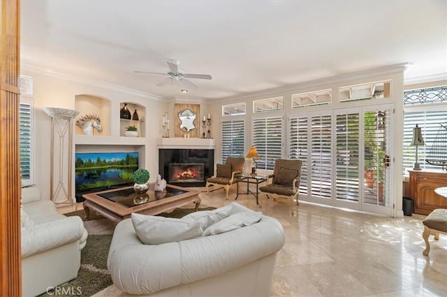 living room featuring built in shelves, crown molding, and ceiling fan