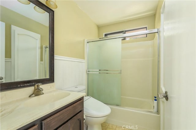 full bath featuring toilet, a wainscoted wall, shower / bath combination with glass door, and vanity