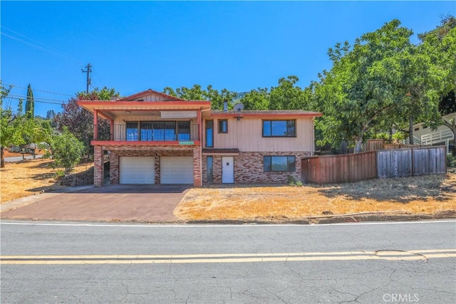 view of front of home featuring aphalt driveway, brick siding, fence, a balcony, and a garage