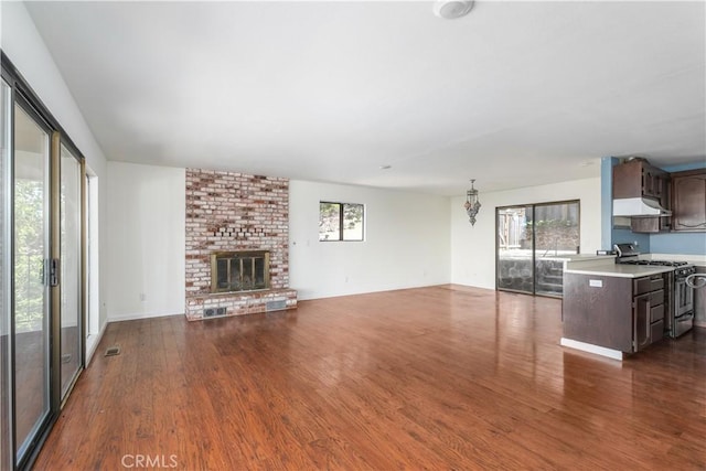 unfurnished living room featuring dark wood-style flooring, a brick fireplace, and visible vents