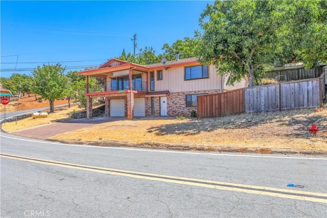 view of front of property featuring driveway, a garage, a balcony, fence, and brick siding