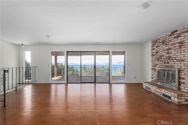 unfurnished living room with a brick fireplace, visible vents, dark wood finished floors, and a wealth of natural light