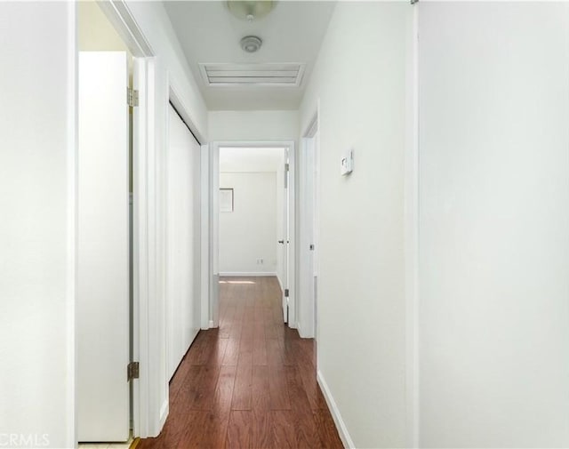 hall with dark wood-style floors, baseboards, visible vents, and attic access