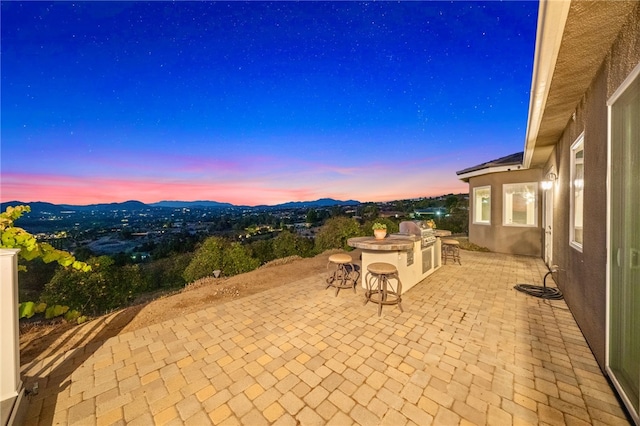 patio terrace at dusk featuring grilling area and a bar