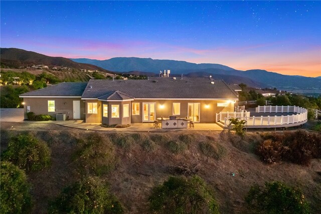 back house at dusk with a patio area, central AC unit, and a mountain view