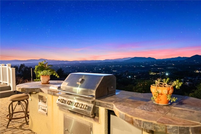 patio terrace at dusk featuring a mountain view, an outdoor kitchen, and a grill