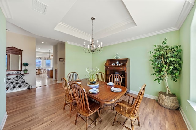 dining room with light hardwood / wood-style floors, a tray ceiling, ornamental molding, and a notable chandelier