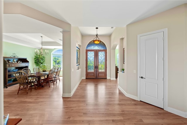 foyer featuring light hardwood / wood-style floors, a raised ceiling, french doors, and an inviting chandelier