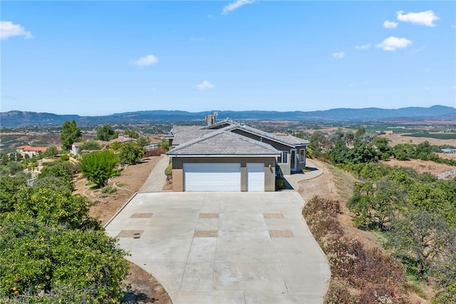 ranch-style home with concrete driveway, an attached garage, a mountain view, and stucco siding