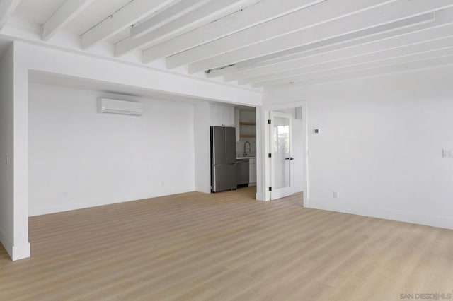 empty room featuring sink, light wood-type flooring, beam ceiling, and a wall unit AC