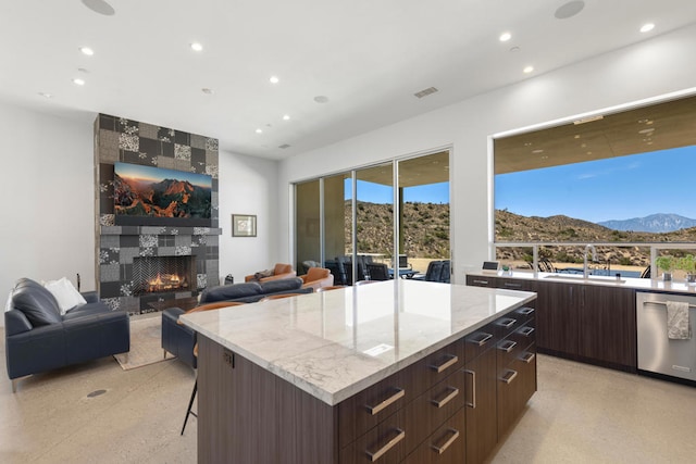 kitchen with a kitchen island, dark brown cabinets, a tiled fireplace, stainless steel dishwasher, and a mountain view