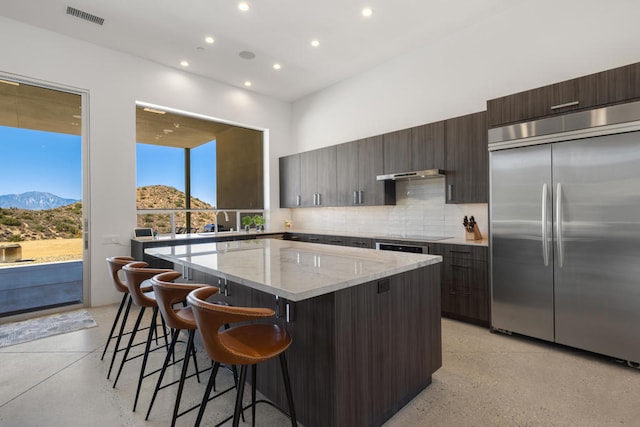 kitchen featuring a mountain view, backsplash, a center island, a kitchen bar, and stainless steel built in refrigerator