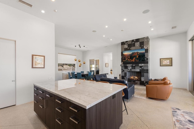 kitchen featuring a large fireplace, dark brown cabinets, a kitchen island, and a kitchen breakfast bar