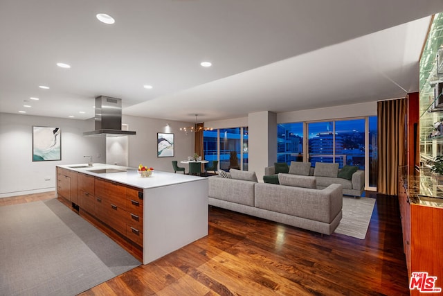 kitchen with sink, a kitchen island with sink, exhaust hood, dark hardwood / wood-style floors, and an inviting chandelier