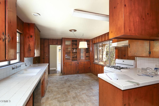 kitchen featuring gas range gas stove, backsplash, wood walls, dishwasher, and tile counters