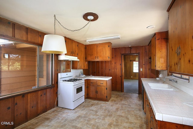 kitchen with hanging light fixtures, wood walls, white gas stove, tile counters, and sink