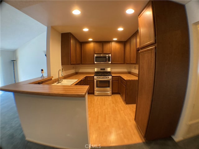 kitchen featuring appliances with stainless steel finishes, kitchen peninsula, sink, and light hardwood / wood-style flooring