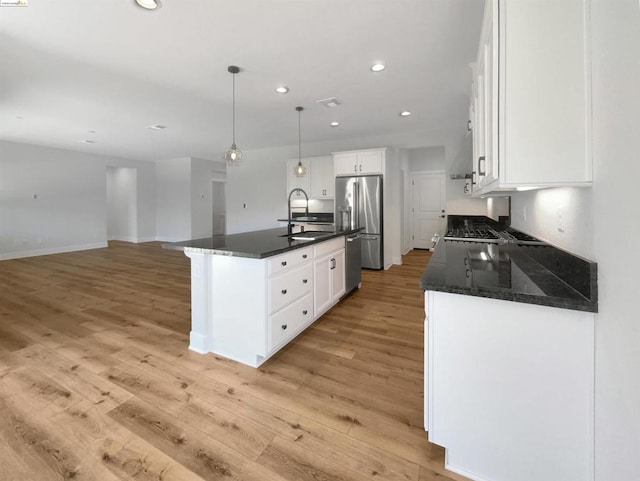 kitchen with white cabinets, stainless steel appliances, a kitchen island with sink, and light hardwood / wood-style flooring