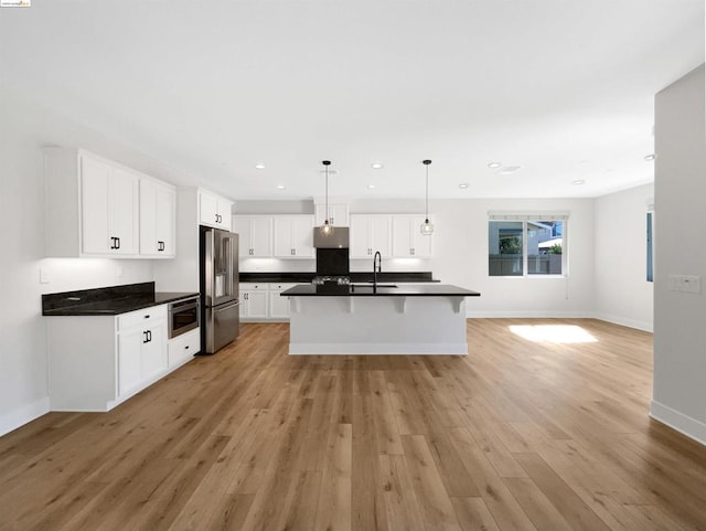 kitchen with appliances with stainless steel finishes, light wood-type flooring, sink, white cabinetry, and hanging light fixtures