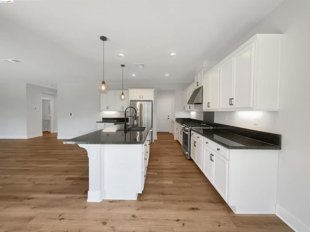 kitchen with light wood-type flooring, stainless steel appliances, a center island with sink, white cabinets, and hanging light fixtures