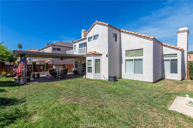 rear view of house featuring ceiling fan, a yard, a balcony, and a patio area