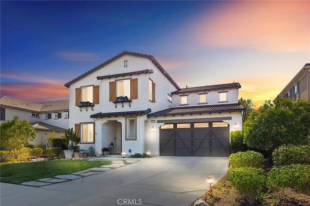 mediterranean / spanish home with a tile roof, stucco siding, an attached garage, and concrete driveway