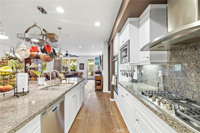 kitchen featuring sink, stainless steel appliances, wall chimney range hood, white cabinets, and light wood-type flooring