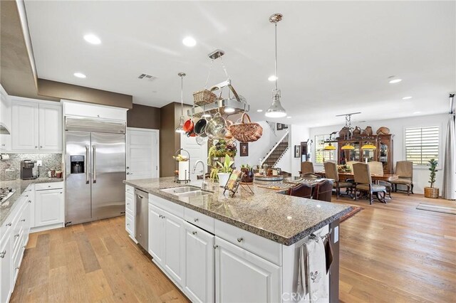 kitchen featuring white cabinets, light wood-type flooring, stainless steel appliances, and an island with sink