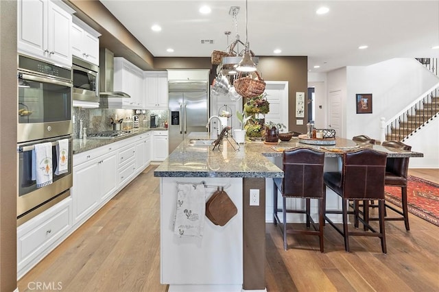 kitchen with built in appliances, white cabinetry, a spacious island, and light wood-type flooring