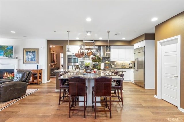 kitchen featuring white cabinetry, a center island, hanging light fixtures, built in fridge, and light hardwood / wood-style flooring