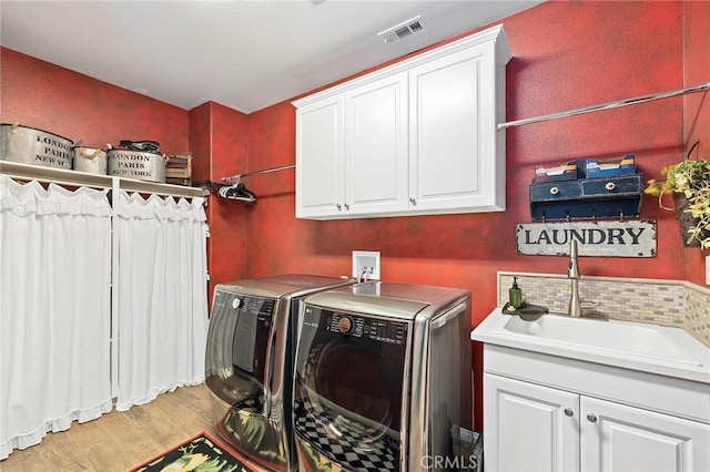 laundry room with washing machine and clothes dryer, light hardwood / wood-style floors, cabinets, and sink