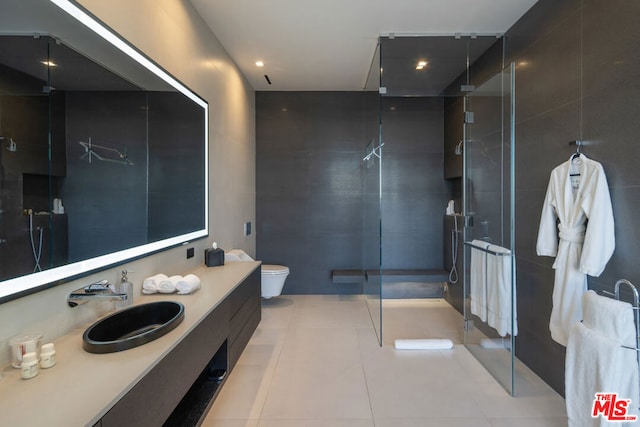 bathroom with tile patterned flooring, vanity, a shower with door, and tile walls