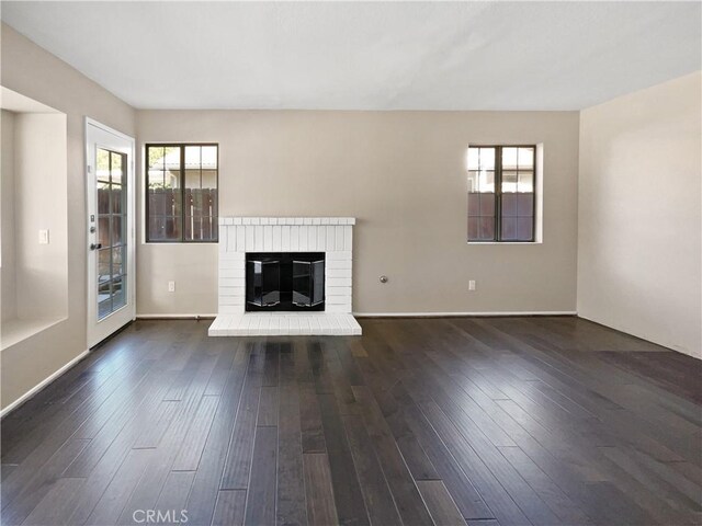 unfurnished living room with a brick fireplace, a wealth of natural light, and dark hardwood / wood-style floors