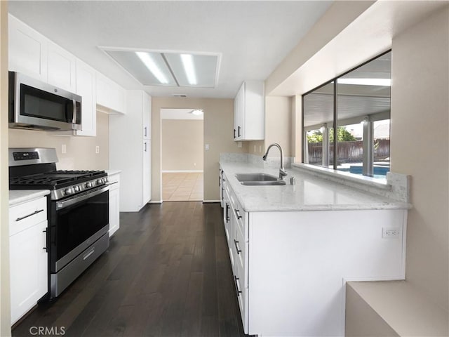 kitchen with appliances with stainless steel finishes, sink, white cabinets, dark hardwood / wood-style flooring, and light stone countertops