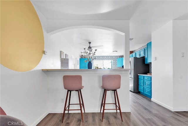 kitchen with light hardwood / wood-style flooring, a breakfast bar, blue cabinets, and kitchen peninsula