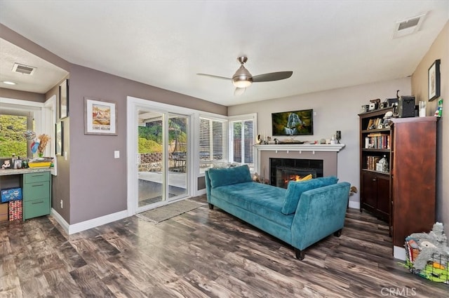 living area with dark wood-style flooring, visible vents, a lit fireplace, and baseboards