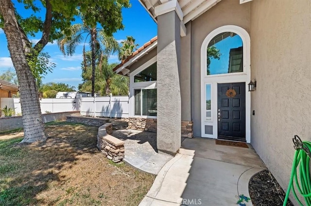 entrance to property with stone siding, fence, and stucco siding