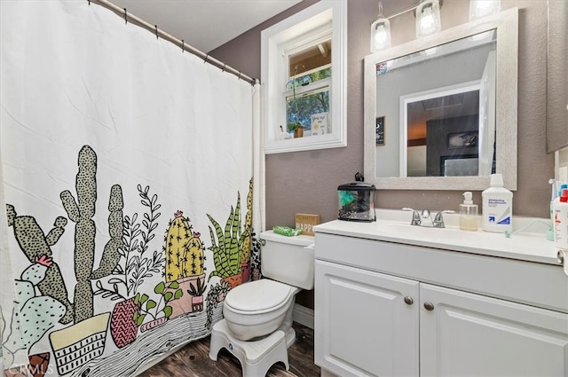 full bathroom with a textured wall, a shower with shower curtain, toilet, vanity, and wood finished floors