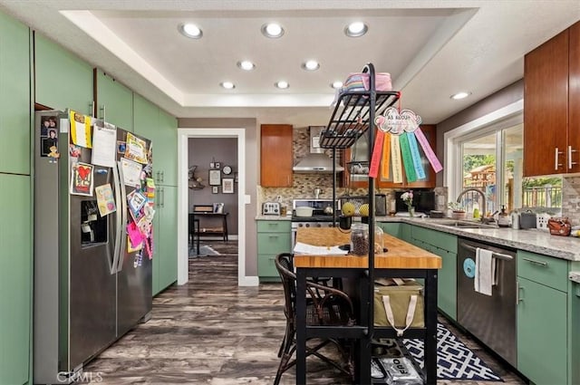 kitchen with a tray ceiling, light countertops, appliances with stainless steel finishes, a sink, and wall chimney range hood